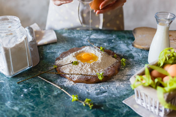 The baker pours the raw egg into the funnel in the flour on the table