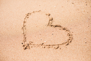 Drawing of a heart on a yellow sand at a beautiful seascape background.