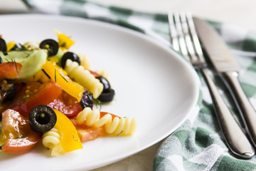 Salad with pasta. On a white plate next to a green checkered cloth