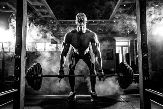 Young shirtless man doing deadlift exercise at gym. Screaming for motivation