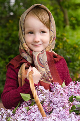 Little girl in a kerchief with a basket of lilac flowers in spring in may