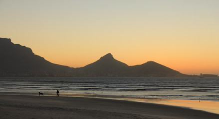 Fototapeta na wymiar Man and dog walking on the beach. Beautiful sunset at Milnerton beach , Cape Town, South Africa.