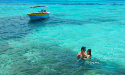 Romantic couple and a boat at a turquoise Caribbean Sea.
