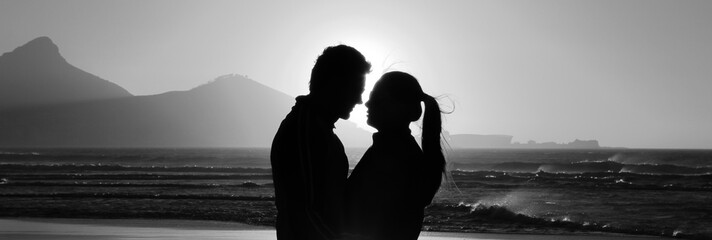 Silhouette of a romantic couple facing each other at Cape Town city, South Africa. Man and woman enjoying sunset on beach. Concept of love and happiness.