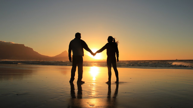 Concept of love and happiness. Silhouette of a romantic couple holding hands on the beach at Cape Town city, South Africa. Man and woman enjoying sunset on beach.