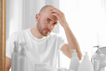 Hair loss concept. Young man looking at mirror