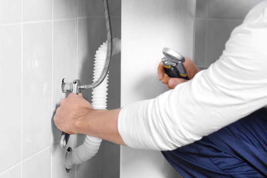 Male hands fixing flexible hose in bathroom, closeup