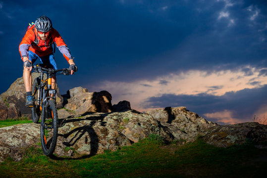 Cyclist Riding Mountain Bike Down Spring Rocky Hill at Beautiful Sunset. Extreme Sports and Adventure Concept.