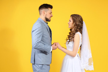 Happy wedding couple holding hands on color background