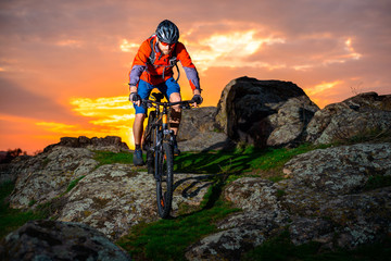Fototapeta premium Cyclist Riding Mountain Bike Down Spring Rocky Hill at Beautiful Sunset. Extreme Sports and Adventure Concept.