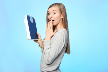 Diet concept. Young beautiful woman holding floor scales on light background