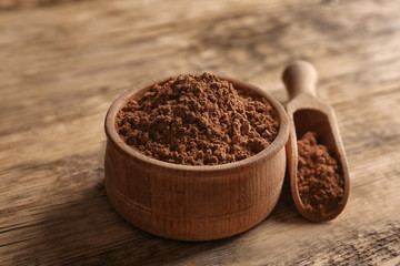 Wooden bowl and scoop with cocoa powder on rustic background