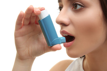Young woman using inhaler during asthmatic attack on white background, closeup