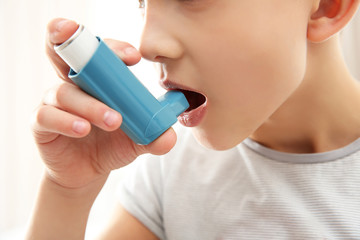 Fototapeta premium Boy using inhaler during asthmatic attack on light background, closeup