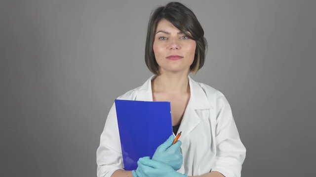 Friendly young nurse holding folder isolated on grey background. Healthcare concept. Shot in 4k.