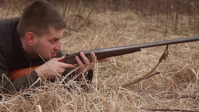 Hunter aiming the hunt during the hunting season. Hunter waiting silently for the hunt during the hunting season. Hunter in camouflage clothes with hunting rifle.