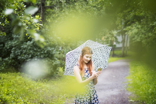 Finland, Pirkanmaa, Tampere, Woman wearing floral dress standing with umbrella in park