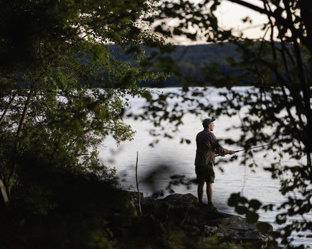 Sweden, Skane, Immeln, Man fishing in lake at sunset