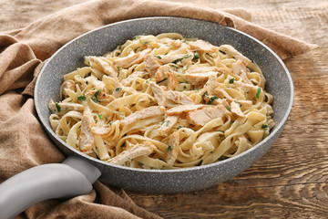 Frying pan with delicious chicken Alfredo on wooden table