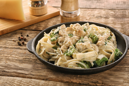 Frying pan with delicious chicken Alfredo on wooden table