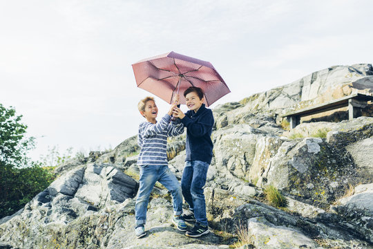 Sweden, Blekinge, Karlskrona, Laughing boys (8-9) with umbrella on rocky hill