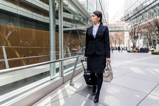 business woman walking by pulling a suitcase near a building