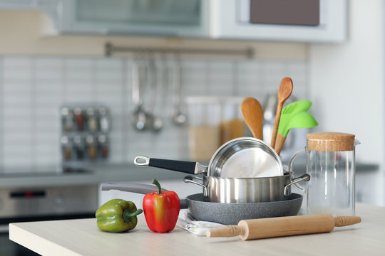 Kitchen utensils, cookware and peppers on wooden table