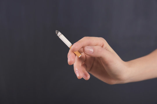Female hand with cigarette on dark background
