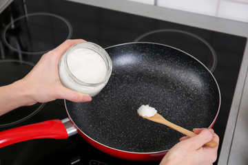 Woman putting coconut oil into frying pan