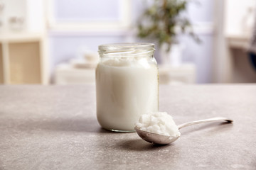Spoon and jar with coconut oil on table