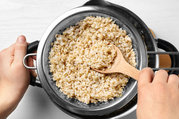 Hand with spoon stirring brown rice in colander on kitchen table