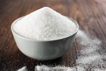 Bowl full of sugar on wooden background