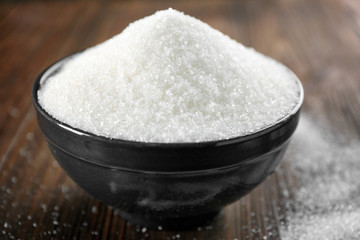 Bowl full of sugar on wooden background