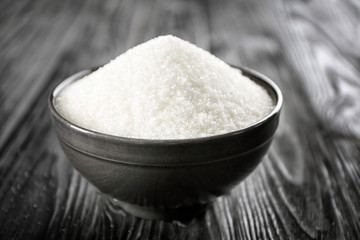 Bowl full of sugar on wooden background