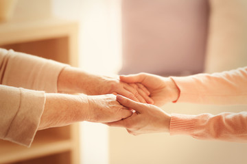 Old and young women holding hands on blurred background, closeup