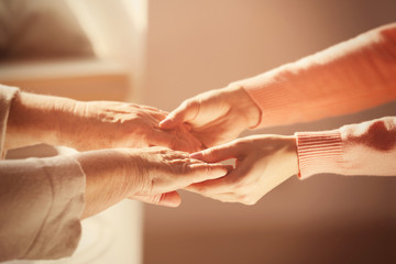 Naklejka premium Old and young women holding hands on blurred background, closeup