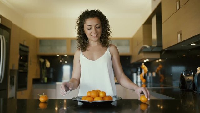 Smiling curly girl making a pyramide from mandarines on the kitchen
