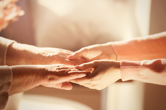 Old and young women holding hands on blurred background, closeup