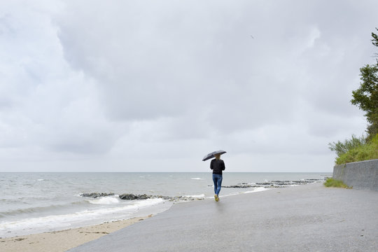 Poland, Niechorze, Woman under black umbrella walking on beach