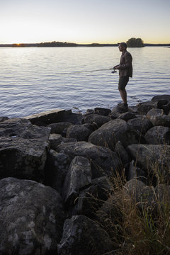 Sweden, Skane, Immeln, Man fishing in lake at sunset