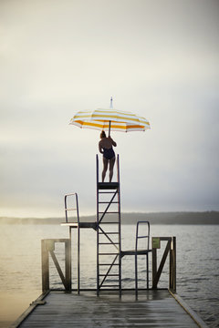 Sweden, Sodermanland, Woman with umbrella standing on ladder by lake