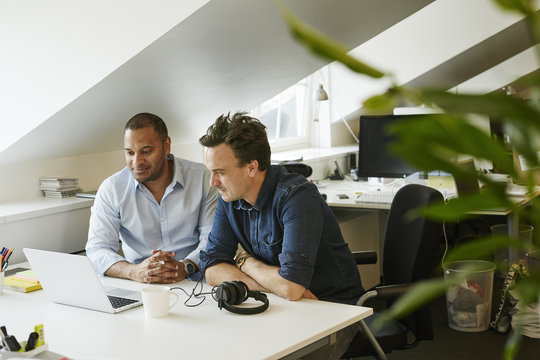 Sweden, Businessmen sitting side by side and looking on laptop in office