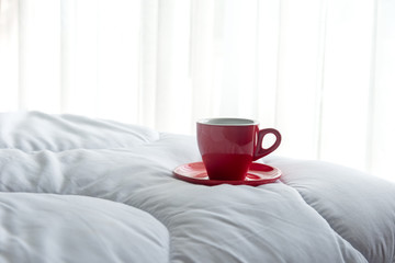 Fototapeta na wymiar Fresh morning coffee in red cup on the bed.