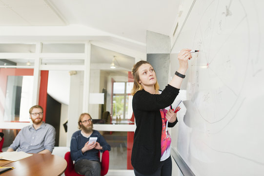 Sweden, Young woman drawing on white board during work meeting