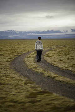 Iceland, Sudurland, Hiker on dirt road through wilderness towards mountain range on horizon