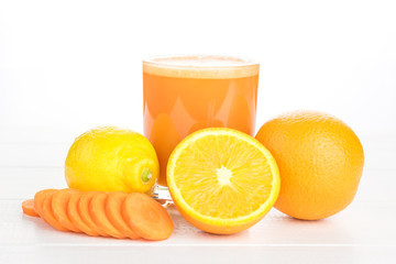 Carrot smoothie with orange and lemon on a white wooden table.