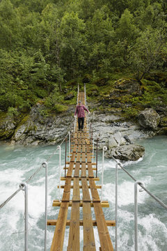 Norway, Jotunheimen, Utladalen, Man walking on suspension bridge over river