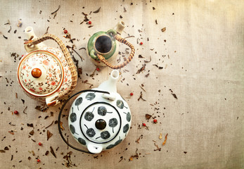 3 various traditional ceramic teapots on a canvas background with copy space. Group of cute steaming clayware pots  with hot tea among tea leaves and berries scattered on fabric