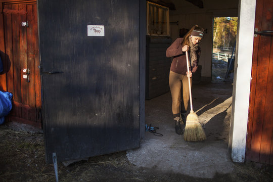 Sweden, Uppland, Faringso, Woman sweeping in barn