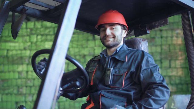 A driver sitting in the loader and smiling in the warehouse.